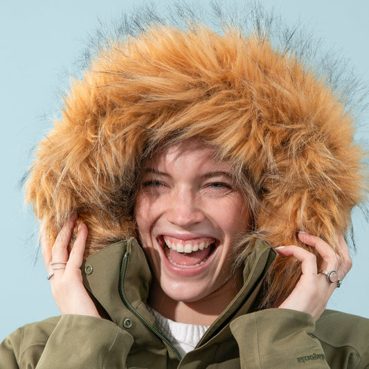 Person wearing a green coat with a large fur hood against a light blue sky