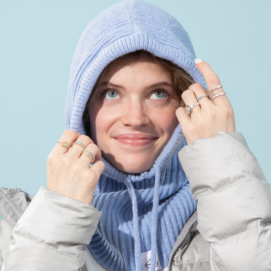 Person wearing a light blue knitted hood and scarf against a light blue background