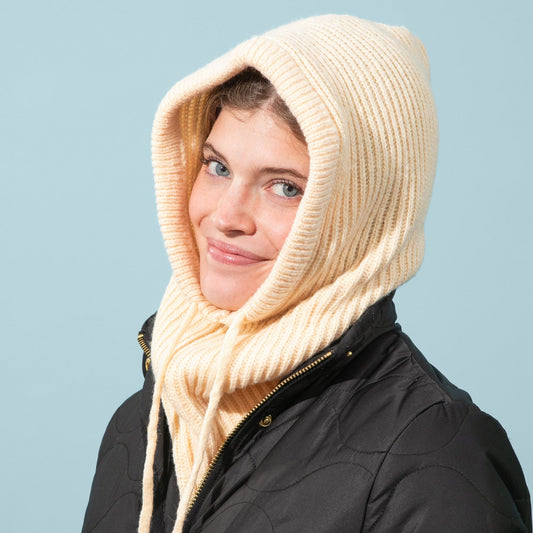 Person wearing a black coat and beige knitted hood against a light blue background