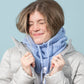 Person wearing a light gray puffer jacket and a blue scarf against a light blue background