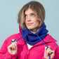 Woman wearing a bright pink jacket and blue knitted cowl against a light blue background