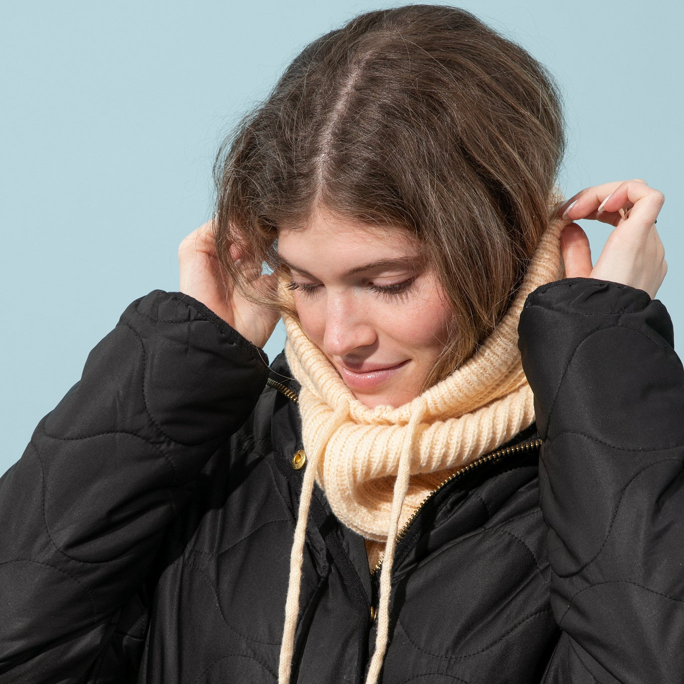 Person wearing a black coat and beige scarf against a light blue background